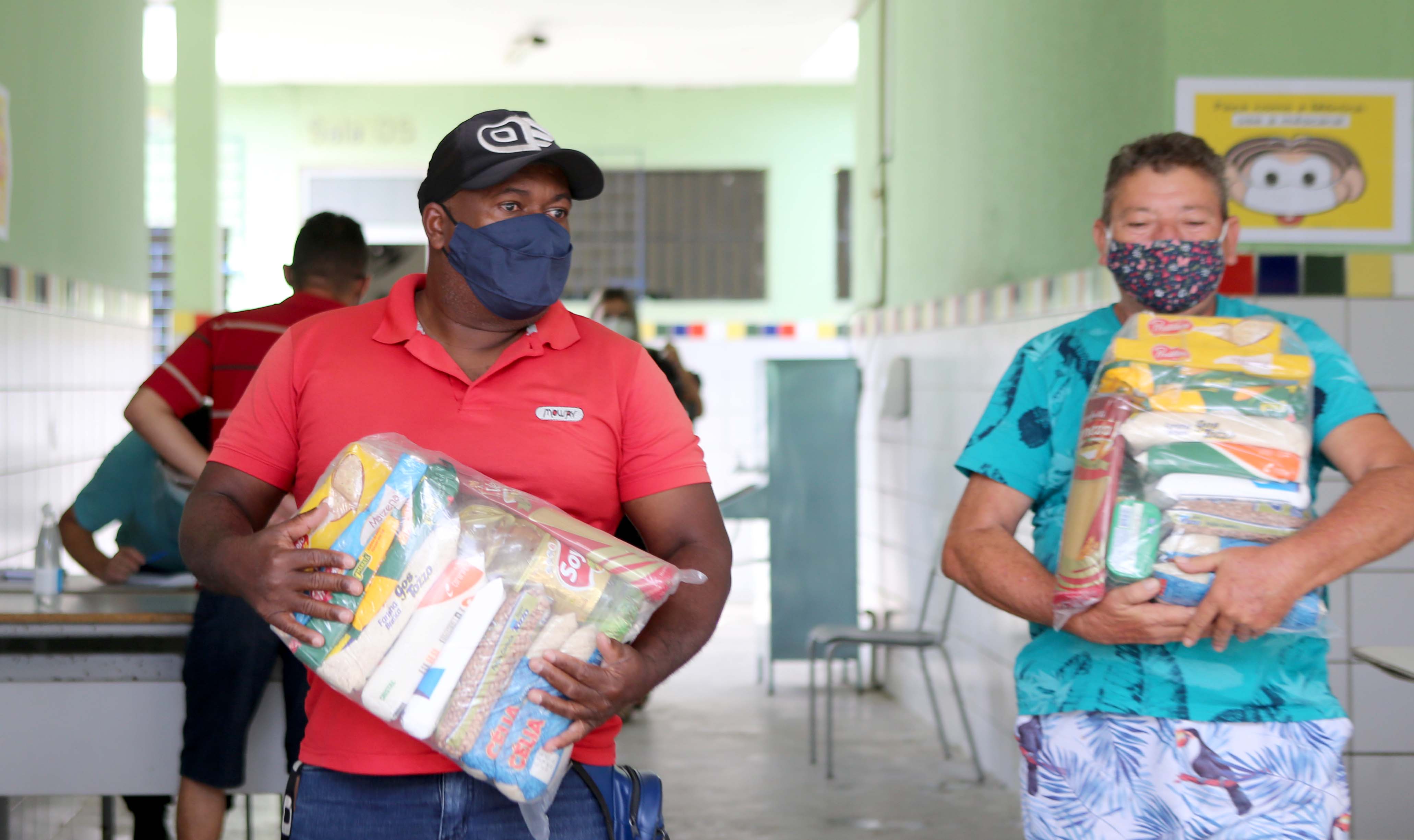 Dois homens de máscaras seguram cestas básicas